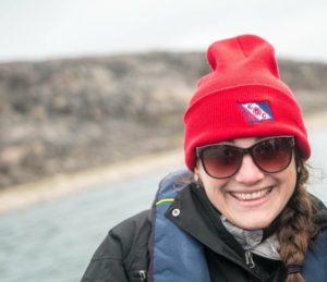 Lacey poses in sunglasses and red hat in front of a lake