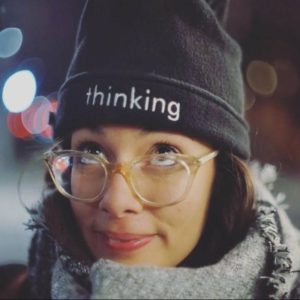 Soley looks up through glasses at her beanie hat which has the work "thinking" embroidered on it.